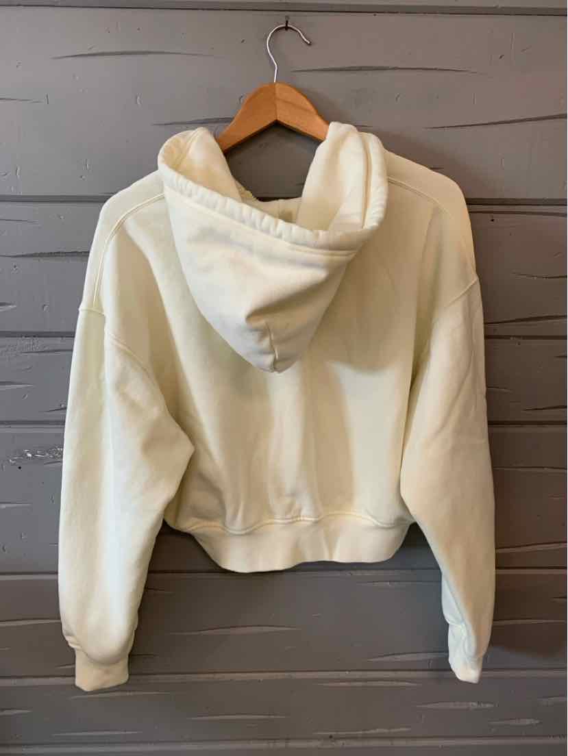 Cream-colored cropped hoodie with a large hood and long sleeves on a wooden hanger.