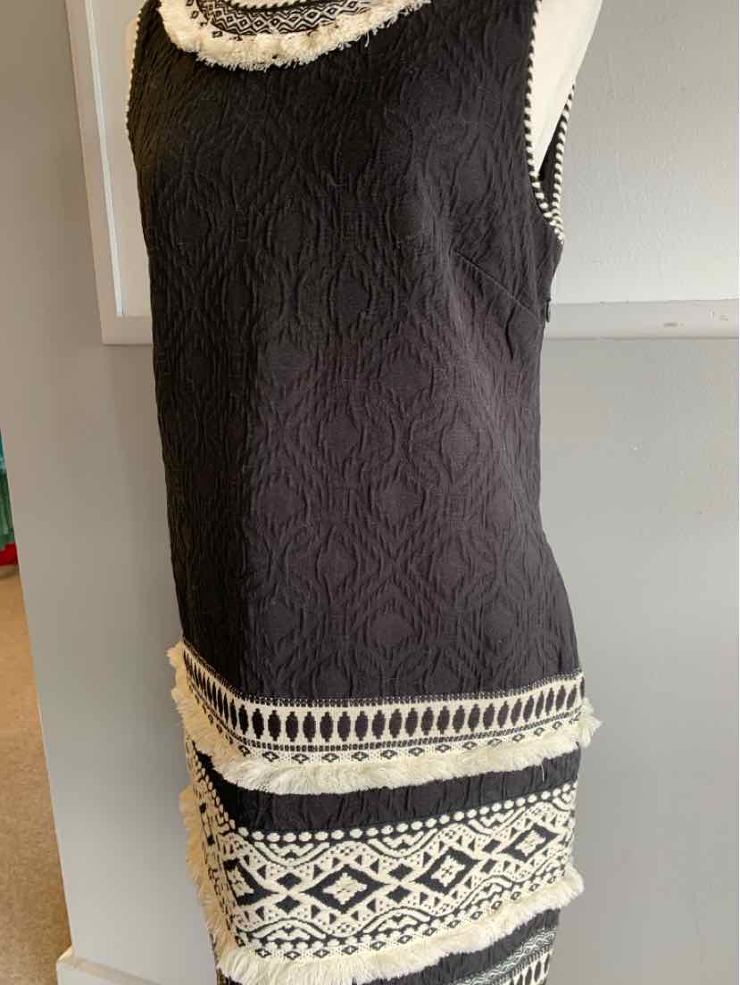 Black sleeveless dress with textured floral embroidery and cream geometric lace trim at hem and pockets.