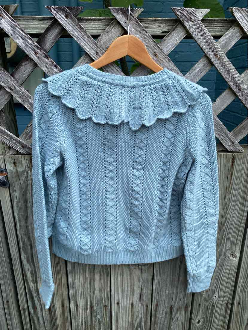Light blue cable knit sweater with scalloped lace collar and long sleeves on wooden hanger.