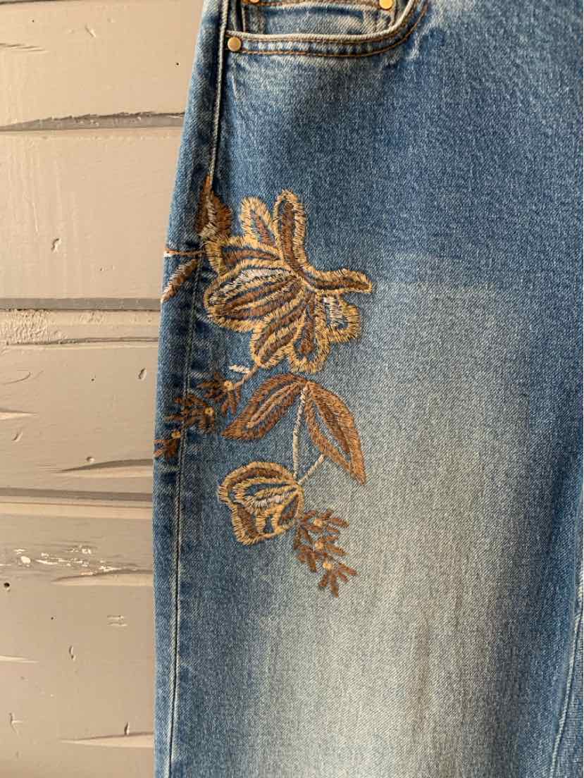 Light blue denim jeans with brown floral embroidery on the upper thigh and pocket area.