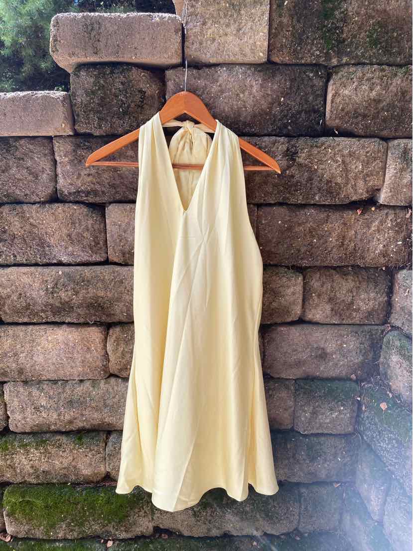 Light yellow sleeveless halter dress with a flowing A-line silhouette on wooden hanger.