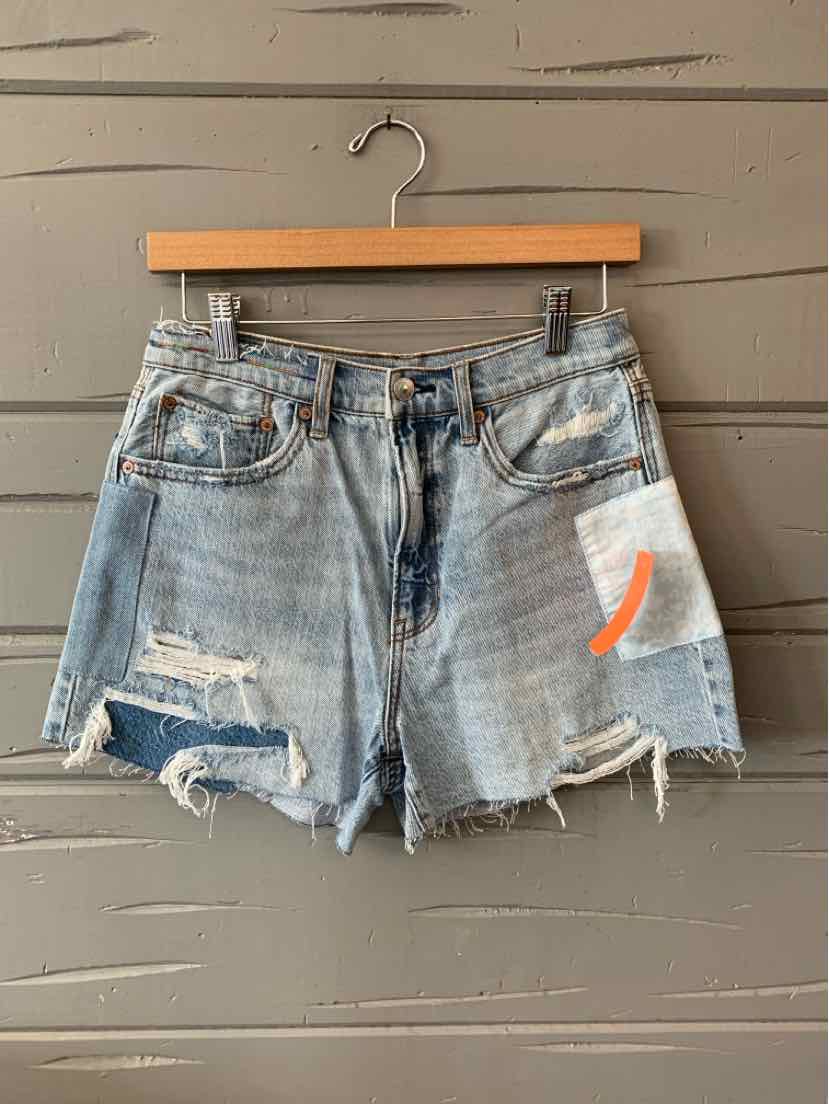 Light blue distressed denim shorts with frayed hems and a white patch featuring an orange design on the right leg.