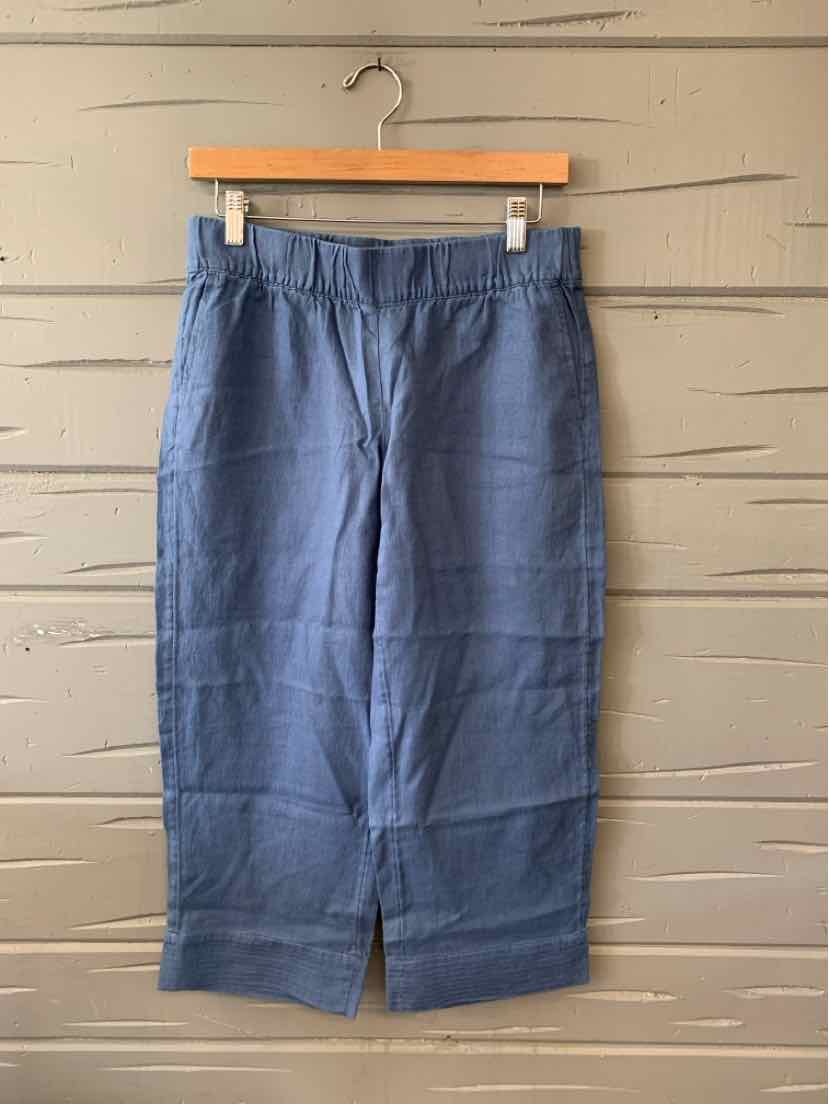 Blue linen cropped pants with front slits and an elastic waistband hanging on wooden hanger.