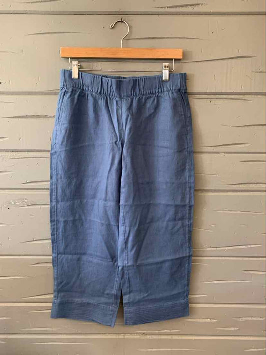 Blue linen cropped pants with front slits and an elastic waistband hanging on wooden hanger.