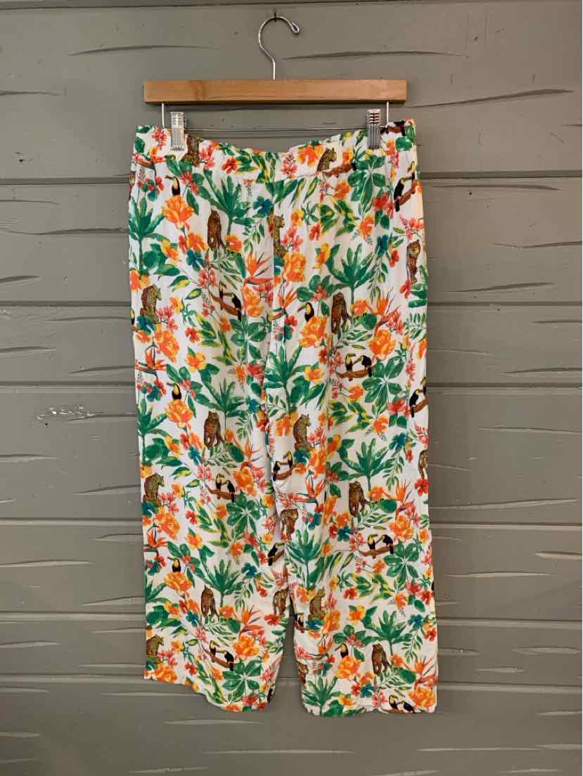 Wide-leg pants with vibrant tropical floral print in green, orange, and white hanging on wooden hanger.