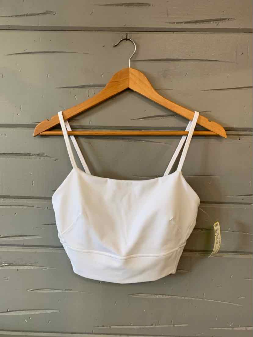 White cropped tank top with thin spaghetti straps and fitted silhouette hanging on wooden hanger against gray wood panel.