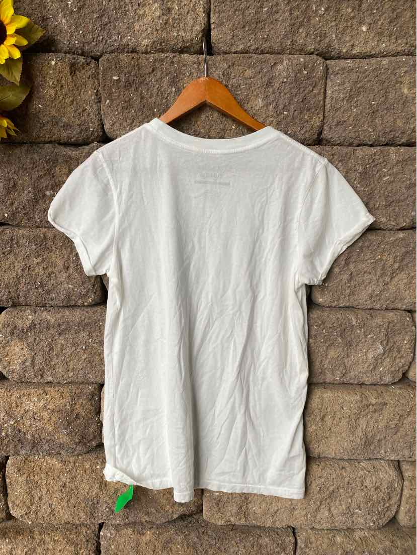 White short-sleeve crew neck T-shirt with regular fit hanging on wooden hanger against stone wall.