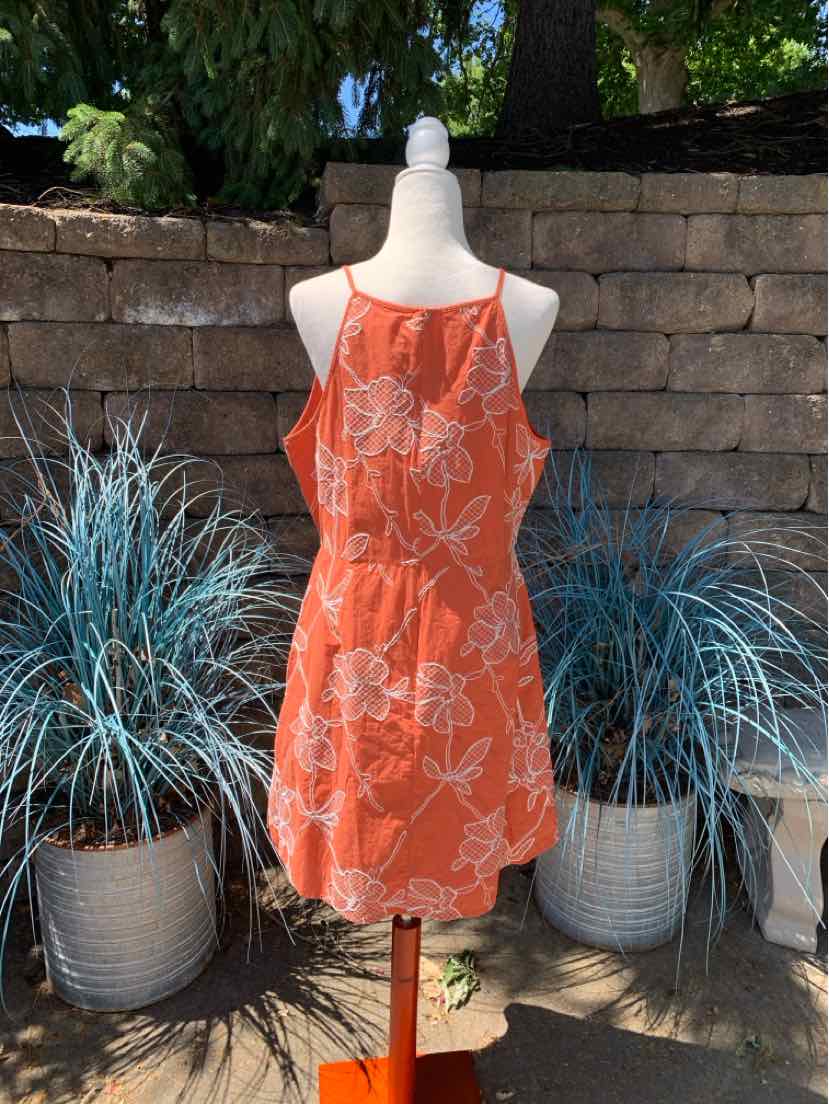 Orange sleeveless dress with white floral print and fitted waist on mannequin outdoors.