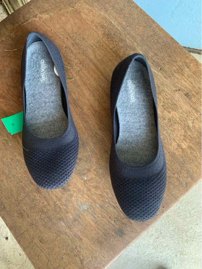 Black knit ballet flats with rounded toes and gray cushioned insoles on wooden surface.