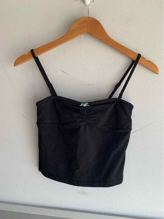 Black cropped camisole with thin adjustable straps on wooden hanger against white wall.