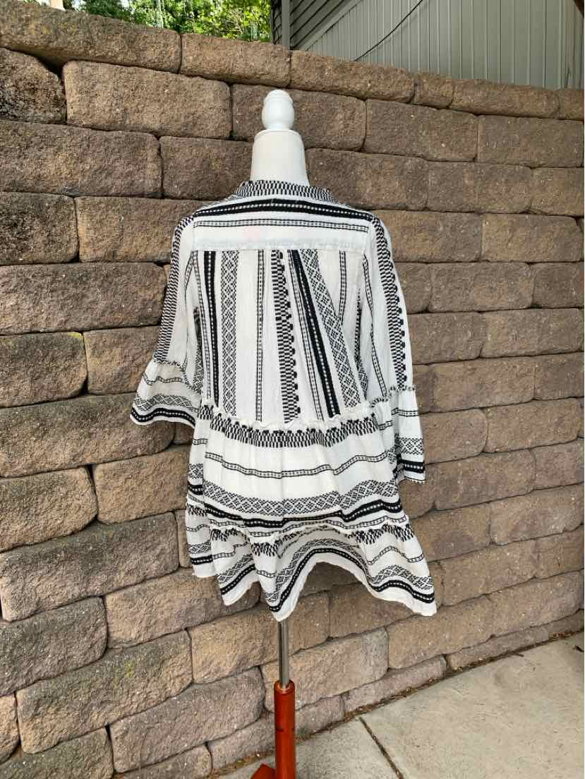 Black and white embroidered blouse with geometric patterns and flowy, asymmetrical hem on a mannequin.