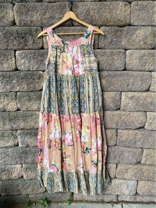 Sleeveless floral midi dress with patchwork design in pink, green, and beige tones hanging against stone wall.