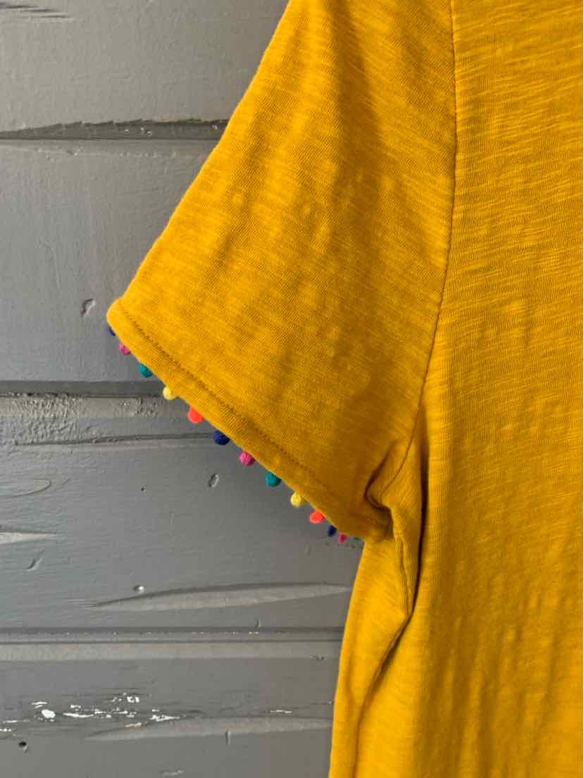 Mustard yellow short sleeve top with multicolored pom pom trim on sleeve edge.