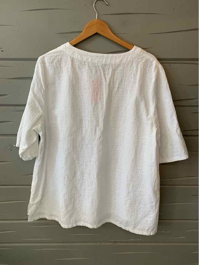 White oversized cotton T-shirt with three-quarter sleeves and a crew neckline hanging on wooden hanger.