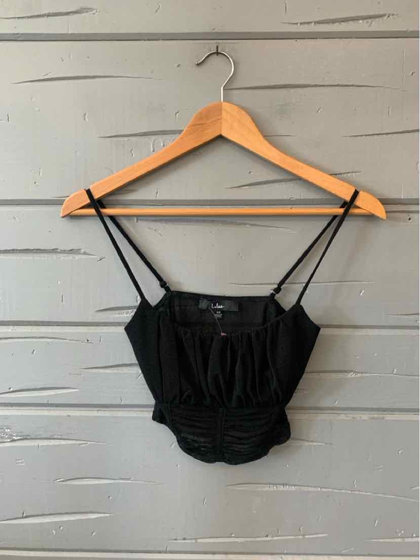 Black cropped camisole top with thin spaghetti straps and ruched front detail on wooden hanger.