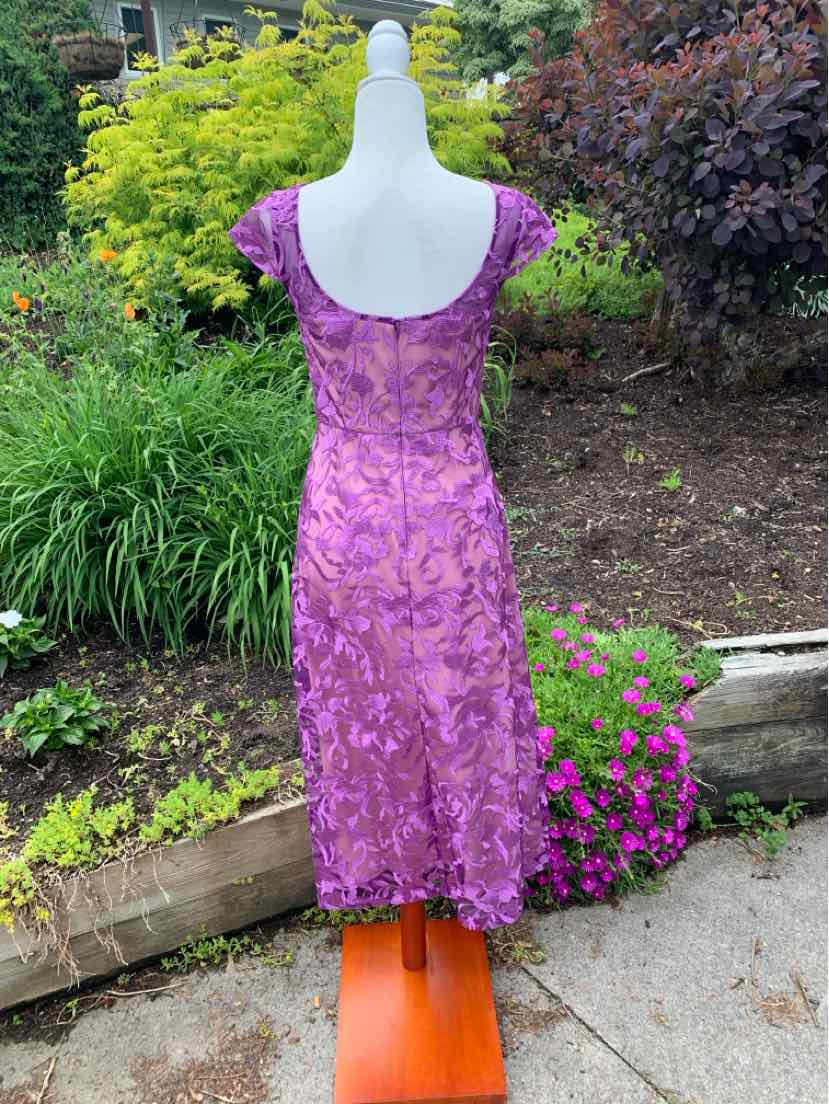 Purple lace dress with scoop back and mid-length hem on white mannequin outdoors.