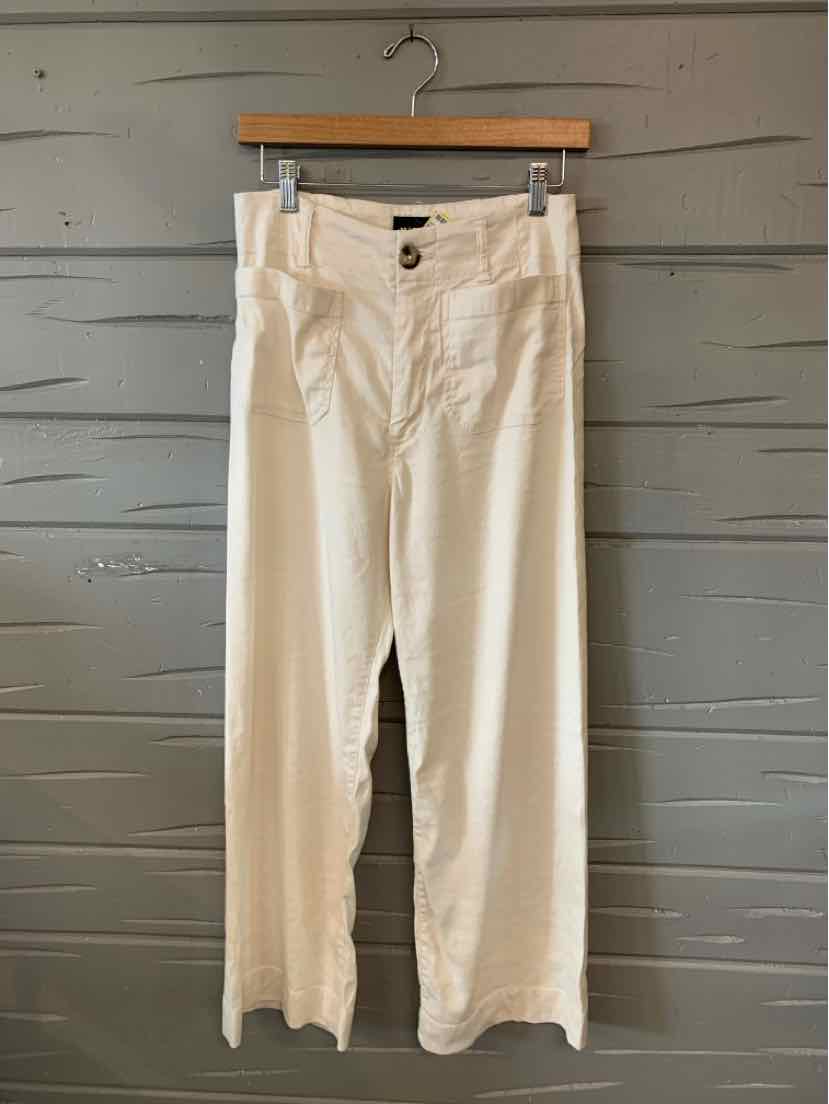 White high-waist wide-leg pants with button and zipper closure hanging on a wooden hanger.