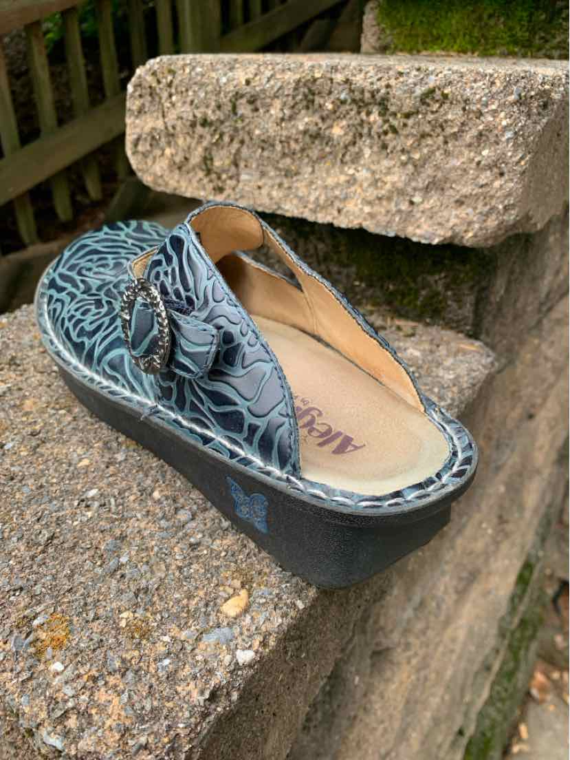 Blue casual slip-on shoe with floral embossed leather upper and cushioned sole.