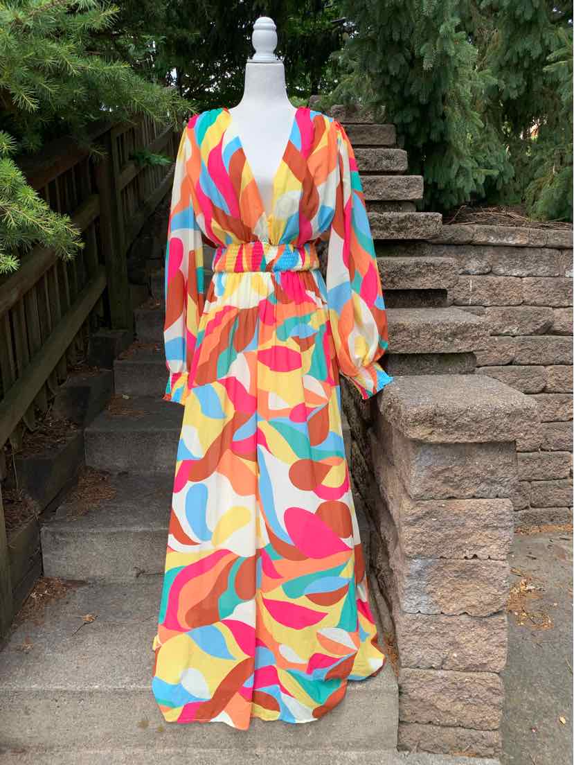 Long-sleeve maxi dress with a colorful geometric print in red, orange, blue, and beige, featuring a deep V-neck and pleated.