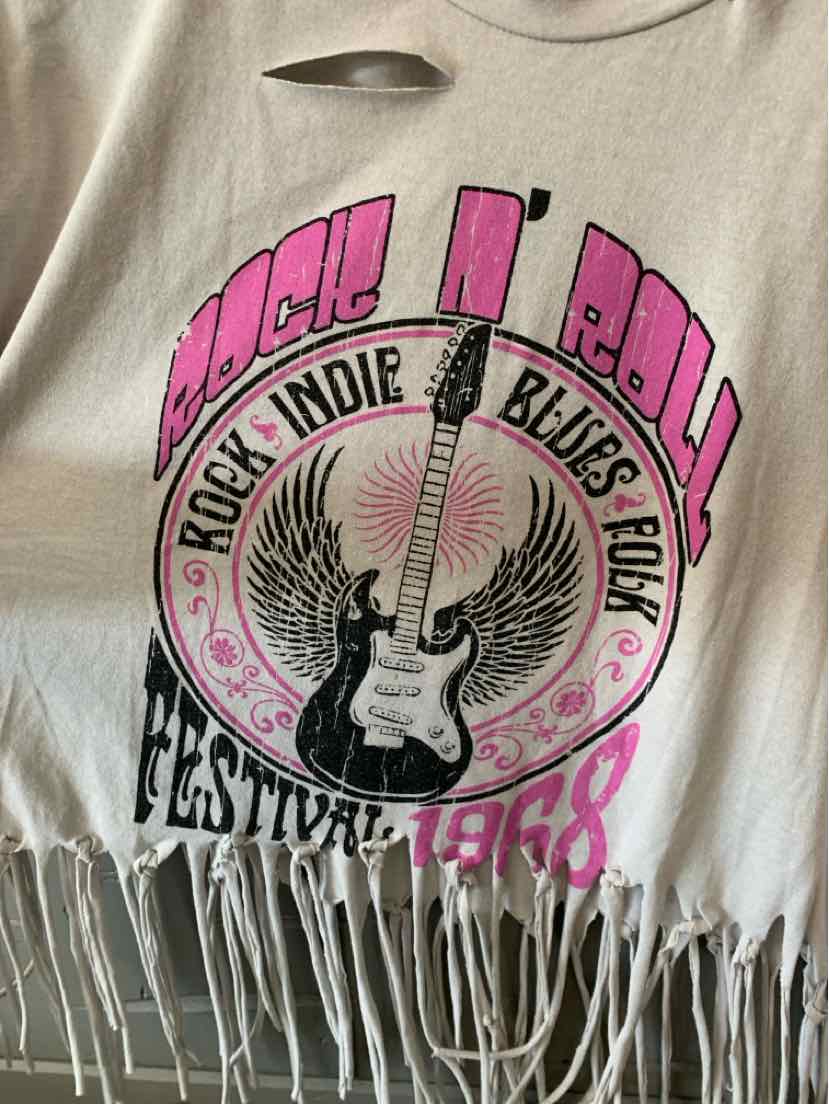 Beige cropped t-shirt with distressed neckline, fringe hem, and pink and black rock and roll graphic featuring a guitar and.