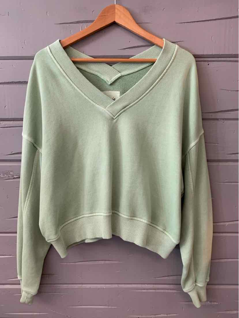 Light sage green long-sleeve V-neck pullover with crisscross back detail and ribbed cuffs.
