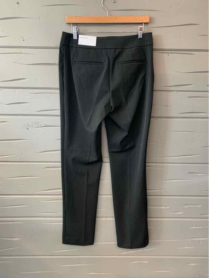 Black slim-fit pants with tailored seams and back pockets hanging on wooden hanger against textured wall.