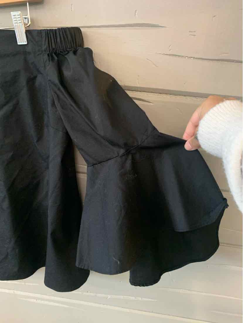 Black skirt with flared ruffle hem and elastic waistband, held by hand against wood panel background.