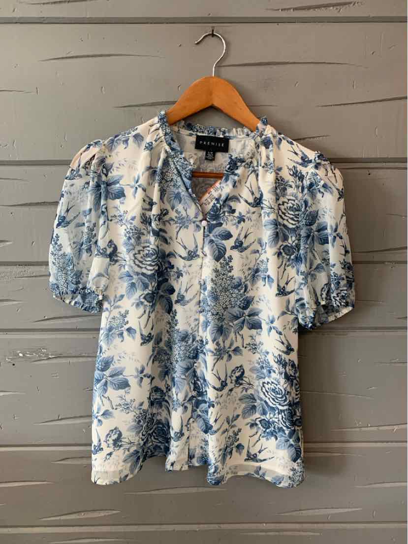 White short-sleeve blouse with blue floral print and V-neckline on wooden hanger.