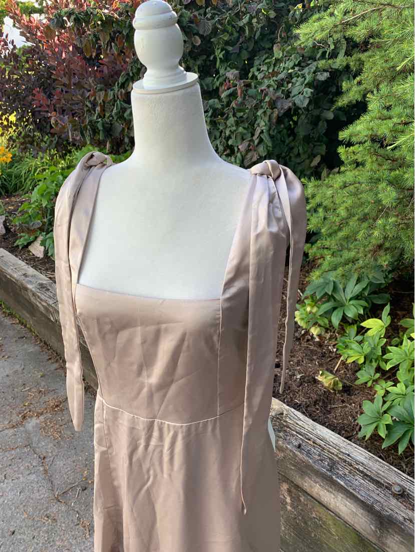 Beige sleeveless dress with square neckline and tied shoulder straps on a mannequin outdoors.