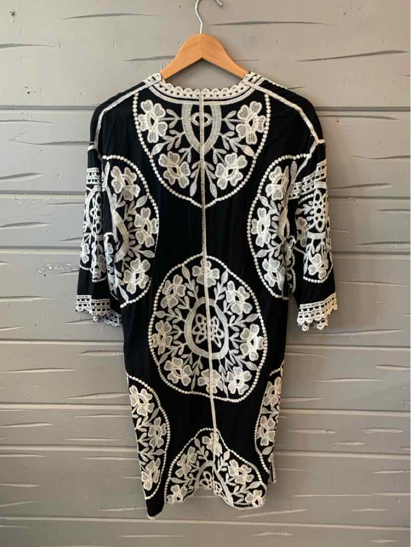 Black knee-length dress with white floral embroidery, three-quarter sleeves, and round neckline.