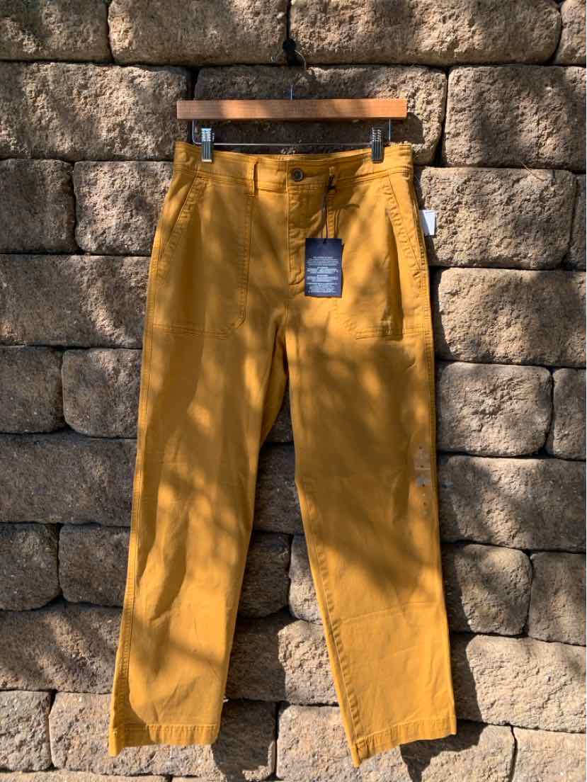 Mustard yellow straight-leg pants with front pockets and button closure hanging against a stone wall.