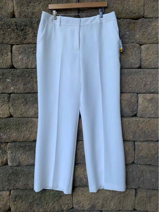 White straight-leg trousers with a high waist and belt loops hanging against a stone wall.