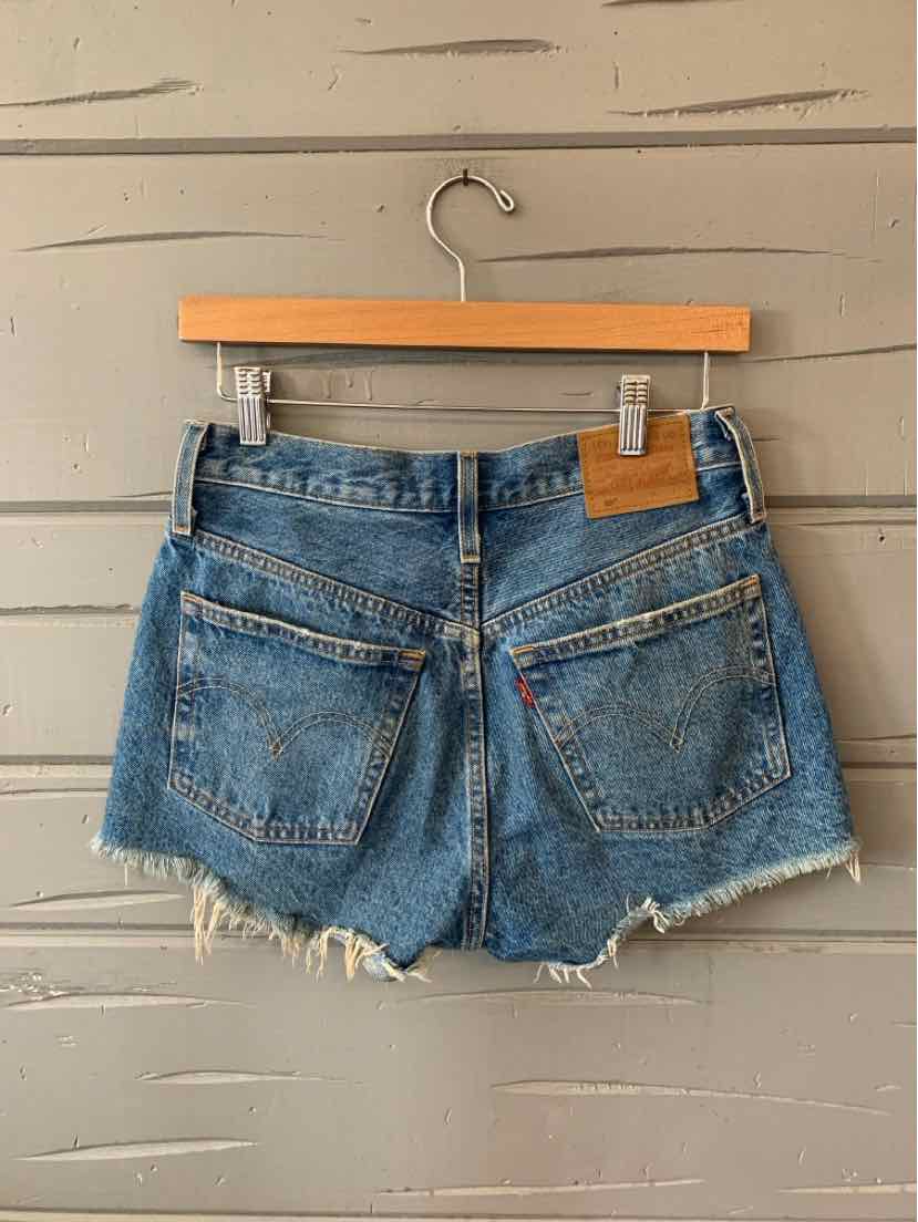 Blue denim Levi's shorts with frayed hems and back pockets hanging on wooden hanger.