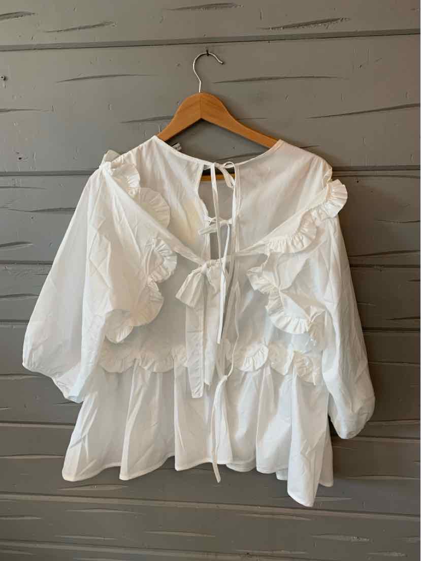 White oversized blouse with puff sleeves, ruffled front, and tie details at neckline and back.