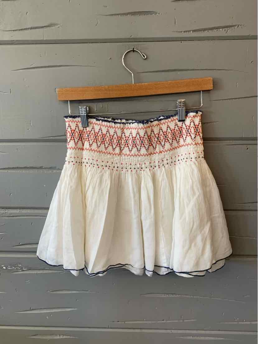 White flowy mini skirt with embroidered pink and orange geometric waistband and gathered fabric detail.