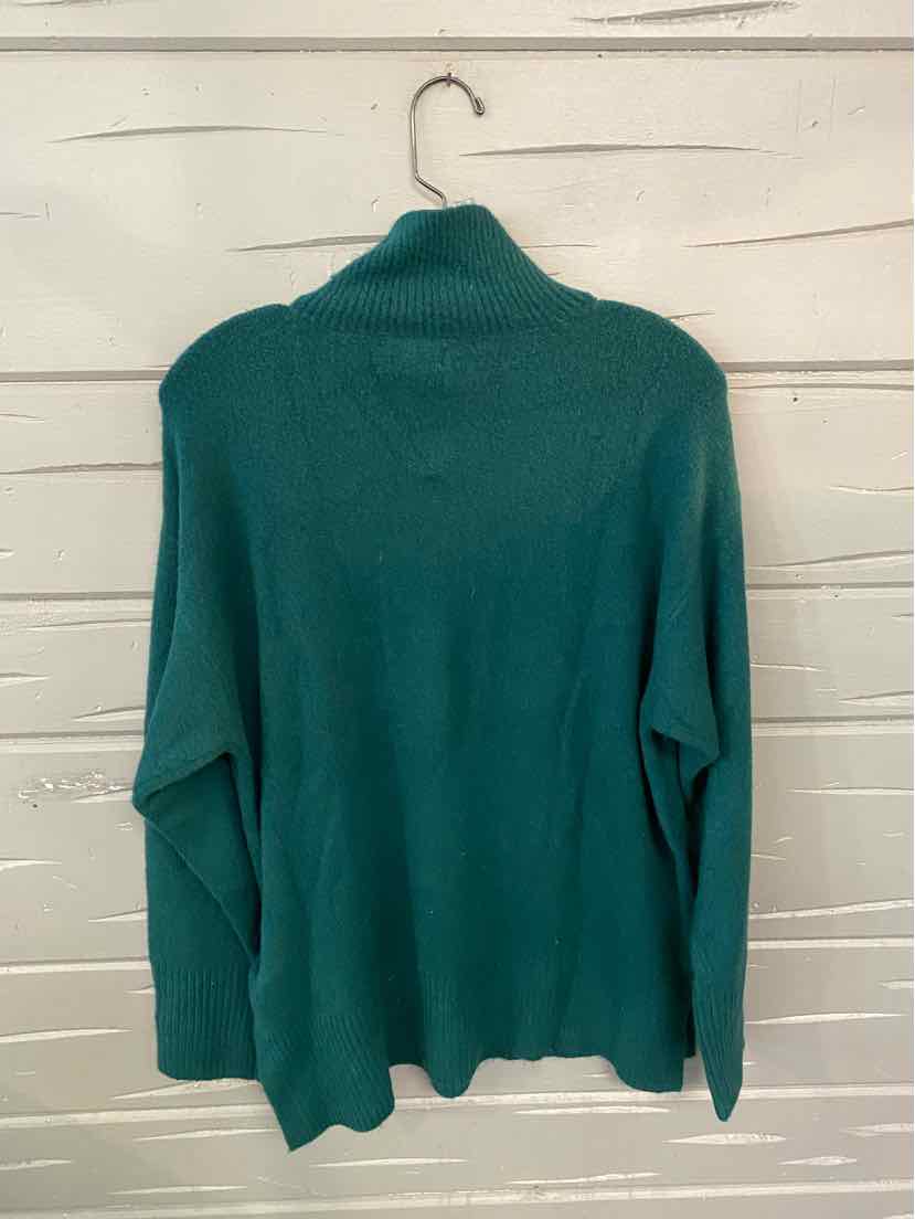 Green long-sleeve crewneck sweater in medium size with a solid knit texture hanging on a wooden wall.