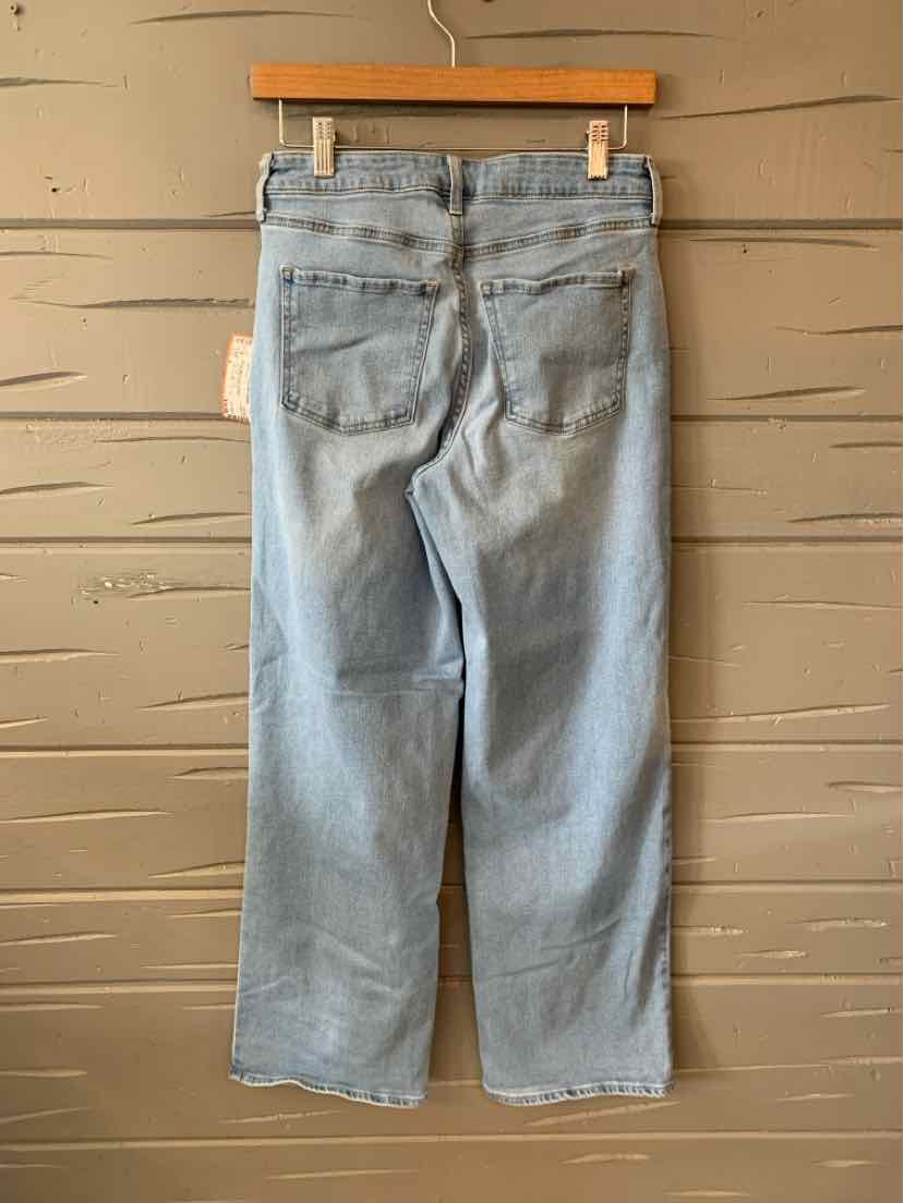 Light blue straight-leg denim jeans with back pockets and belt loops hanging on wooden hanger.