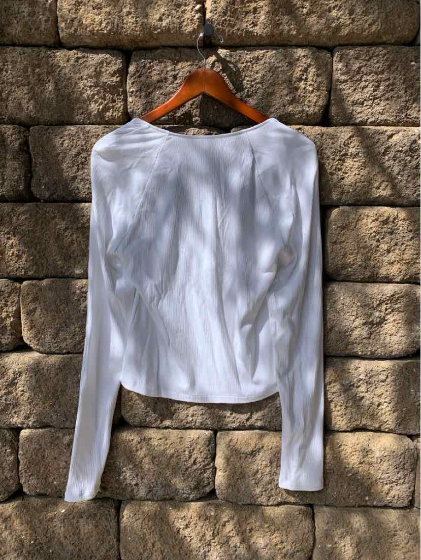 White long-sleeve fitted t-shirt with crew neck on wooden hanger against stone wall background.
