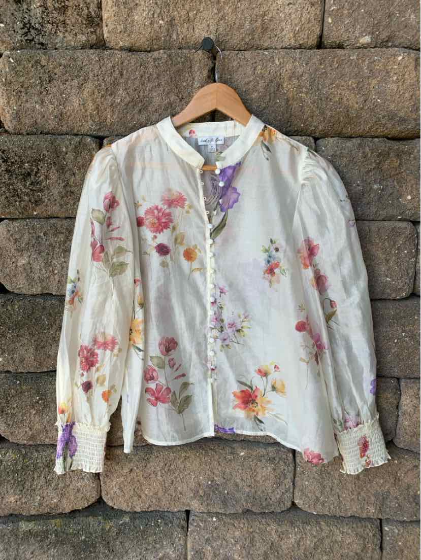 White semi-sheer blouse with pink and orange floral print, puffed long sleeves, ruffled cuffs, and button-up front with.