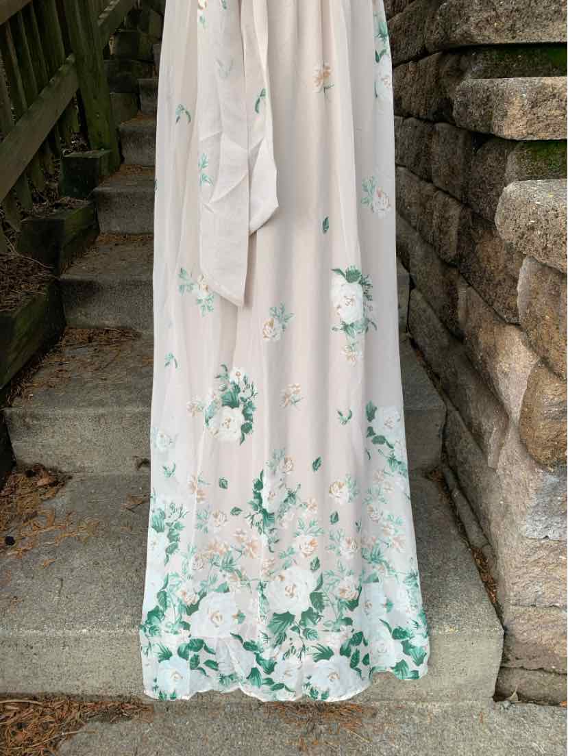 Beige maxi dress with green and white floral print and long sash belt on stone steps.