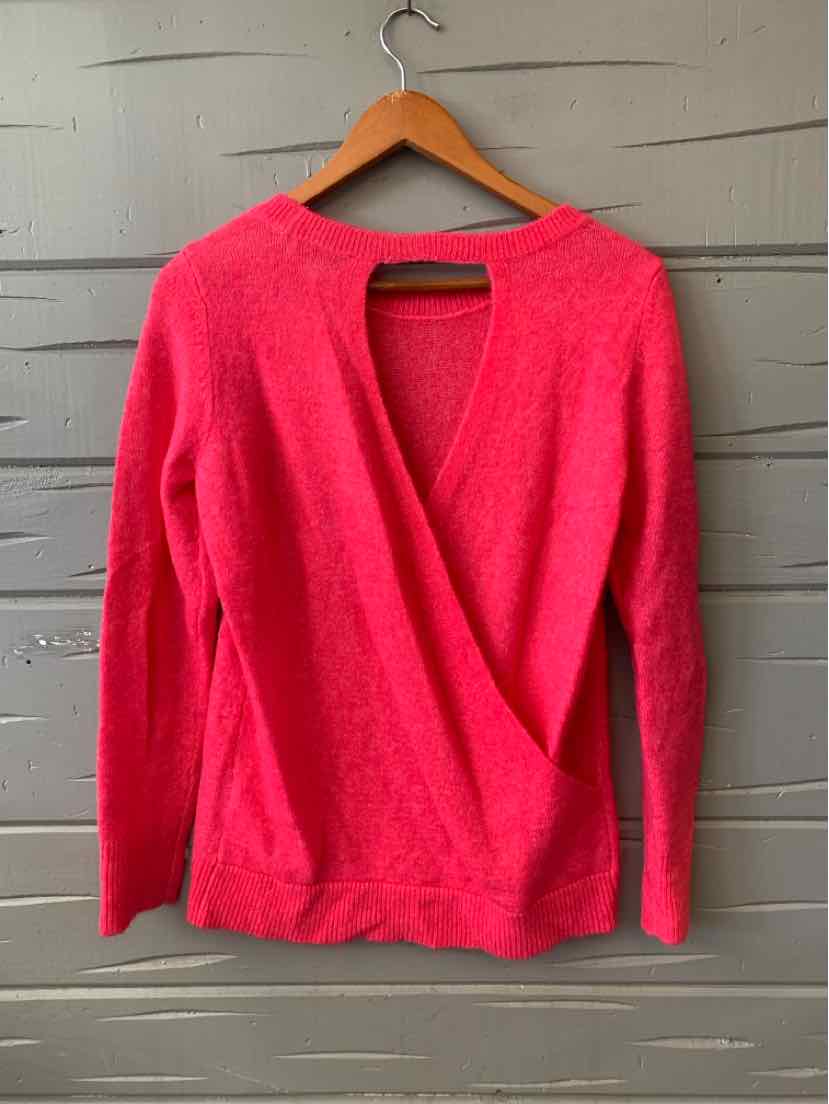 Bright pink long-sleeve sweater with V-neck and soft knit fabric hanging on wooden hanger.