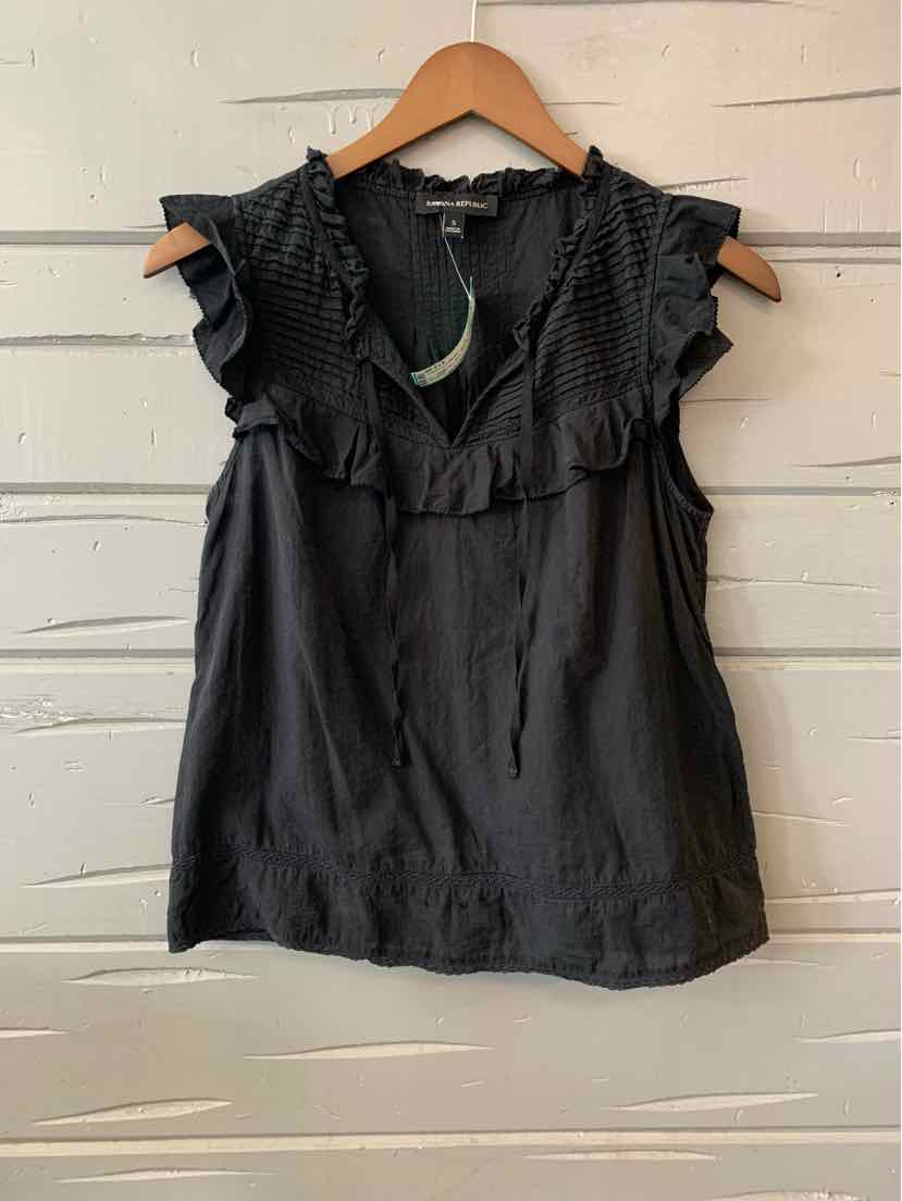 Black sleeveless blouse with ruffled V-neck and lightweight fabric hanging on wooden hanger.