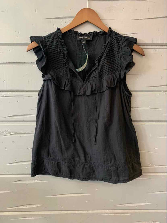 Black sleeveless blouse with ruffled V-neck and lightweight fabric hanging on wooden hanger.