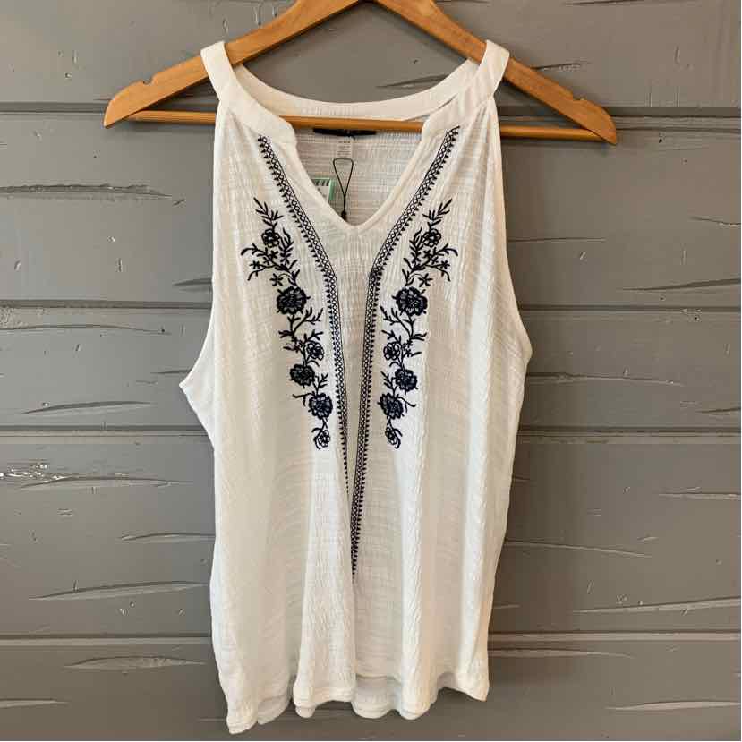 White sleeveless tank top with black floral embroidery and scoop neckline on wooden hanger.