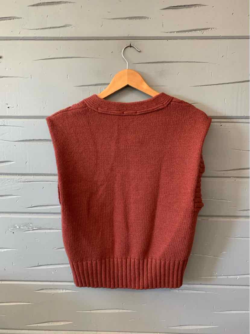 Rust-red sleeveless knit sweater vest with a crew neck and ribbed hem, hanging on a wooden hanger.