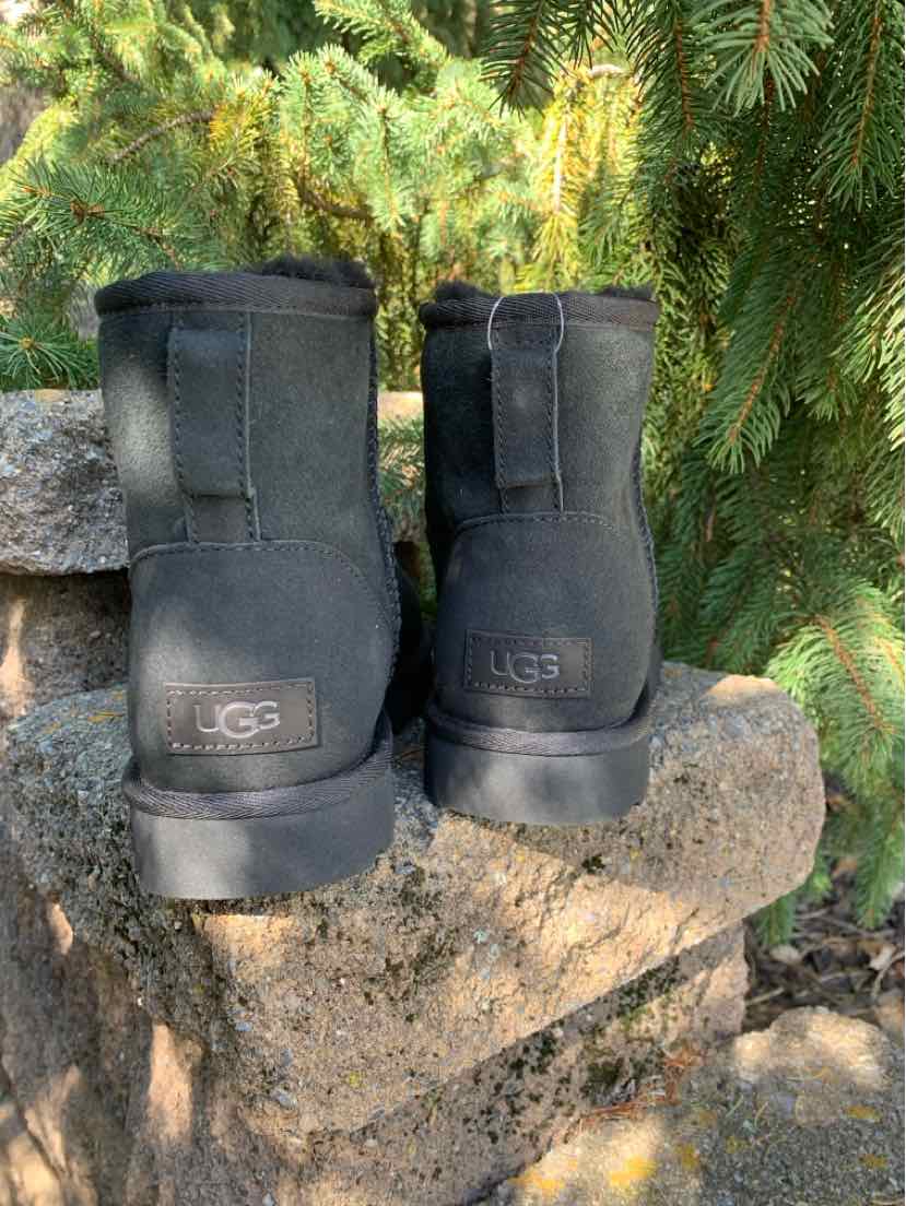 Black suede UGG ankle boots with rounded toes, pull tabs, and logo patches, shown from the back.