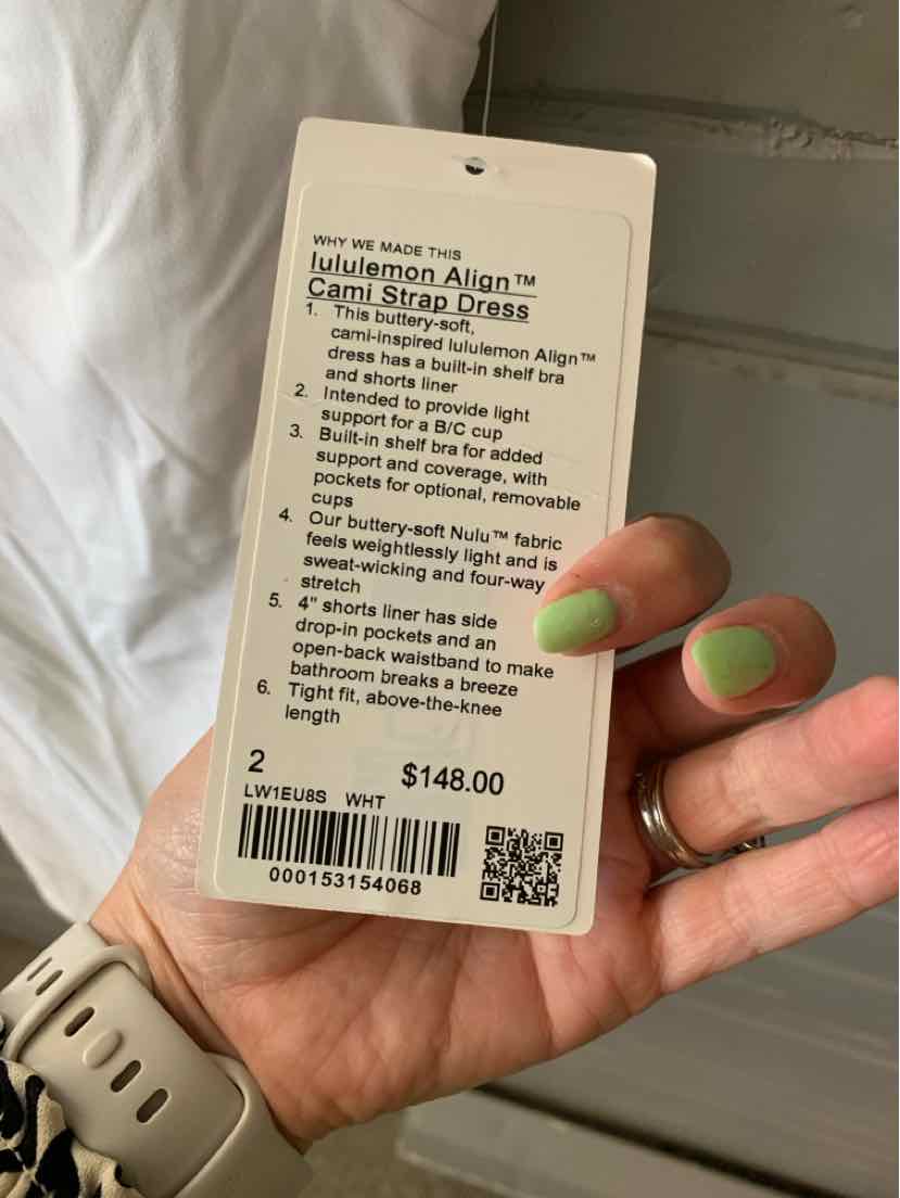 White rectangular clothing tag with black text showing Lululemon Align Tee Size 2 and price $148, held by a hand with.