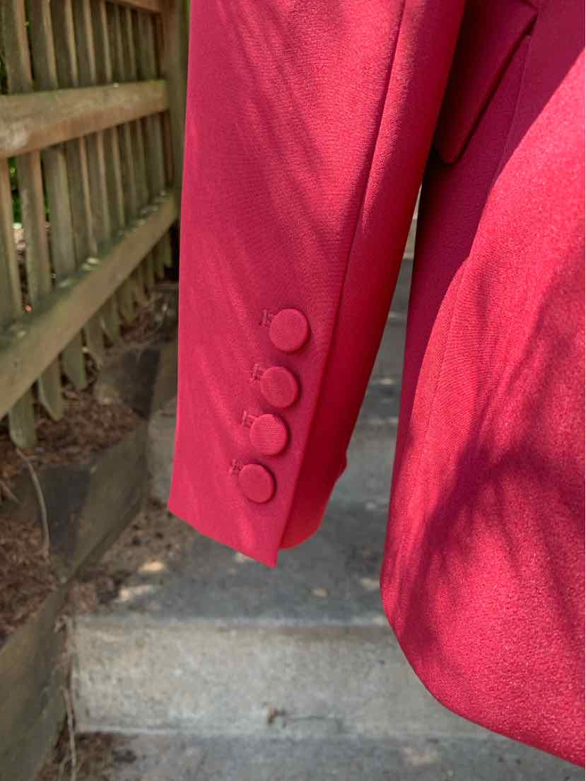 Red blazer sleeve with four matching fabric-covered buttons in a smooth, tailored design.