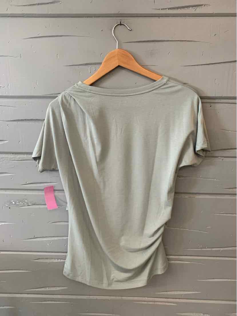 Light sage green short-sleeve women's top with ruched side detail hanging on wooden hanger.
