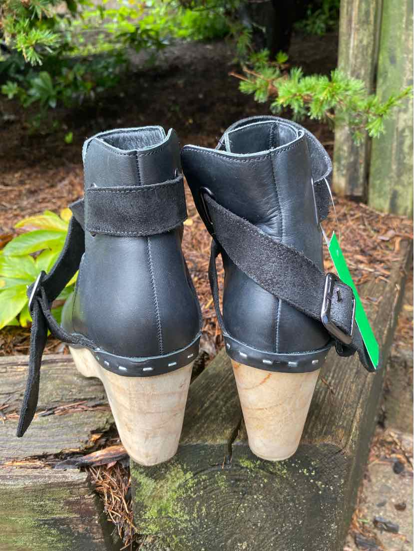 Black leather ankle boots with wooden stacked heels and wrap-around straps with stud detailing.